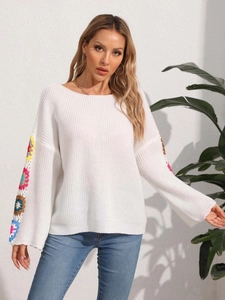 Detail of colorful crochet floral patchwork on a white knit sweater sleeve