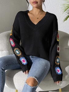 Detailed view of colorful handmade crochet floral patterns on black knit sweater sleeves