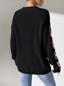 Detail of colorful hand-crocheted floral patchwork on black knitted sweater sleeve