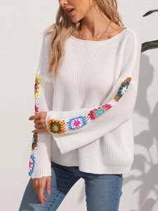 Detail of white knit sweater featuring colorful crochet floral patterns on long sleeves
