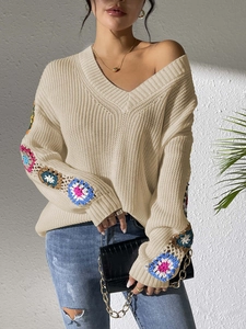 Detail of handmade crochet floral patterns on beige V-neck knitted sweater sleeves