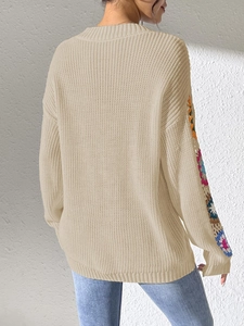 Close-up of beige knit sweater with colorful crochet patchwork on sleeves and texture