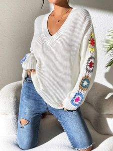 Detail of V-neck white knit sweater featuring colorful crochet flower patchwork sleeves