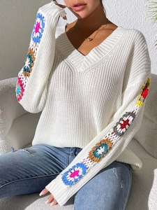 Macro shot of colorful floral crochet sleeve detail on a white V-neck knit sweater