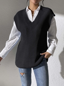 Detail shot of a black V-neck knitted vest layered over a white long sleeve shirt and jeans