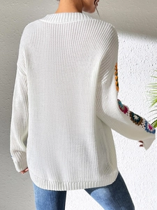 Rear view of a white knit sweater featuring colorful crochet patchwork on the sleeves