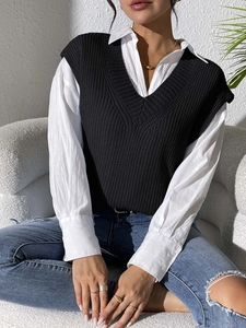 Detail of a black V-neck knitted vest layered over a white long-sleeve button-up shirt