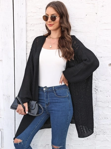 Close-up of black chunky knit cardigan paired with white top and ripped blue jeans