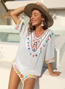 Détail de la broderie ethnique et du col en V à pompons sur une robe de plage blanche