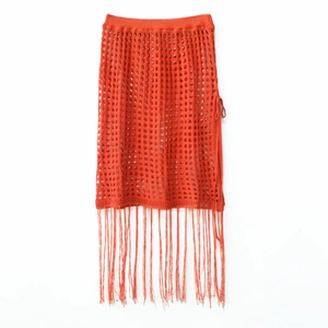 Detail of orange crochet knit skirt featuring hollow-out patterns and long fringe tassels