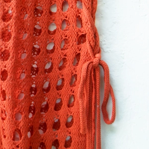 Close-up of orange hollow-out knit beach skirt featuring side lace-up details