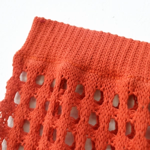 Macro detail of bright orange knit fabric with ribbed edges and hollow crochet mesh design