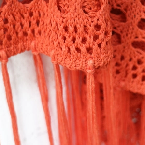 Detail of orange crochet knit skirt featuring intricate hollow patterns and long fringes