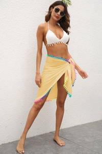 Détail d'un sarong d'été avec franges à pompons et haut de bikini au crochet avec coquillages