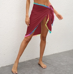 Détail d'une jupe de plage bordeaux avec pompons colorés et fermeture nouée latérale