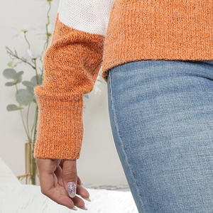 Dettaglio ravvicinato di un maglione in maglia grossa bicolore arancione e bianco con polsini