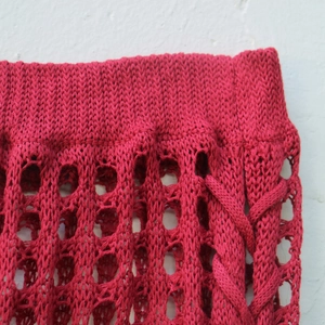Detail of dark red knit skirt featuring ribbed waistband and hollow crochet patterns