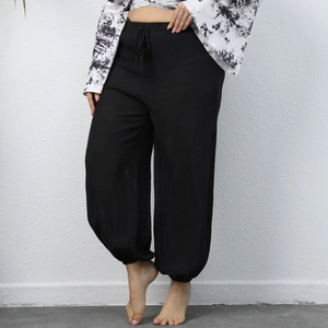 Detail of high-waisted black harem pants featuring textured fabric and elastic drawstring waist