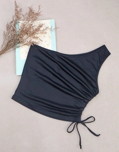 Flat lay of black one-shoulder cropped top with side drawstring and bow detailing