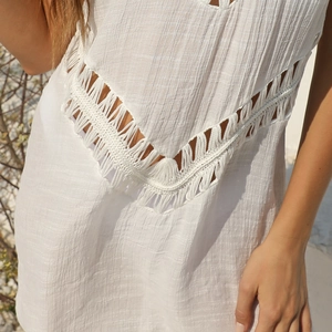 Detail of white crochet V-neck beach dress with bohemian fringe tassels and textured fabric