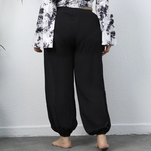 Rear view of black loose-fit harem pants and marble print bell-sleeve top on a model