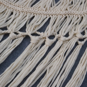 Détail macro du nouage macramé fait main beige et des franges souples de la robe