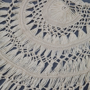 Détail du motif au crochet fait main avec des franges denses sur une robe de plage beige