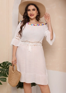 Close-up of bohemian white dress showing colorful pom-poms and intricate hollow lace details