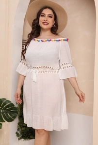 Detail of bohemian white off-shoulder beach dress with colorful pom-poms and tassels