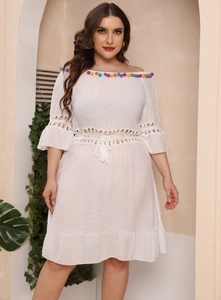 Detail of colorful pom-pom trim and lace patchwork on a white off-shoulder beach dress