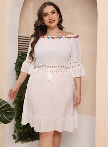 Detail of white boho dress showing colorful pom-poms on neck and lace crochet patterns