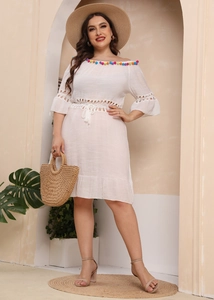 Detail of colorful pom-poms and delicate lace stitching on a white off-shoulder beach dress