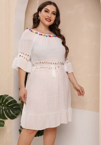 Detail of white off-shoulder dress with colorful pom-poms and intricate crochet patterns