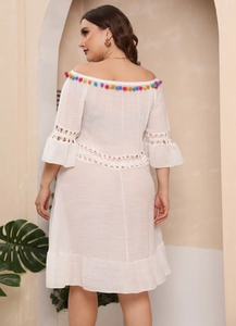 Detail of white off-shoulder beach dress featuring colorful pom-poms and bohemian lace crochet