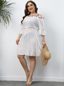 Detail of white off-the-shoulder beach dress with colorful pom-pom trim and crochet lace