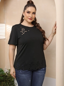 Détail du motif rose évidé au laser et de l'ourlet ondulé sur un t-shirt noir grande taille