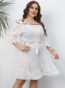 Detail of white off-shoulder beach cover-up featuring colorful pom-pom trim and tassels