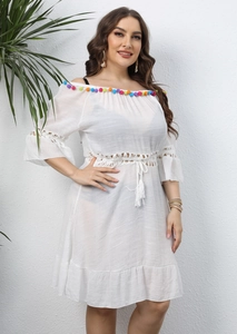 Detailed view of white off-shoulder beach dress with colorful pompom trim and lace waist