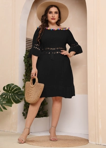 Detail of off-shoulder black beach dress with colorful pompoms and crochet lace sleeves