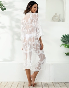 Dettaglio di un copricostume in pizzo bianco con ricami floreali e trama in mesh