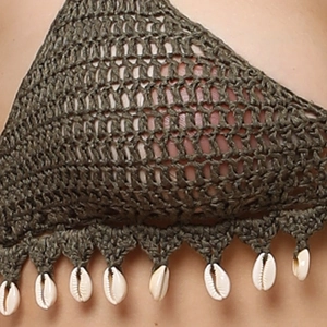 Macro detail of olive green crochet fabric with bohemian shell charms and tassels