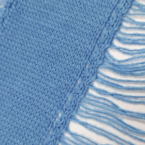 Close-up of light blue knit fabric showing intricate texture and long fringe tassels