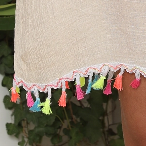 Detail showing white lace hem and vibrant colorful tassels on a beige beach dress