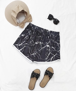 Flat lay of marble print summer shorts with straw hat and sunglasses for vacation