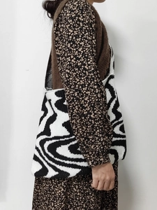 Side view of woman carrying a black and white wave pattern knitted tote bag on shoulder