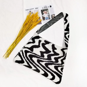 Detailed knit texture of a black and white wavy pattern shoulder bag on white fabric