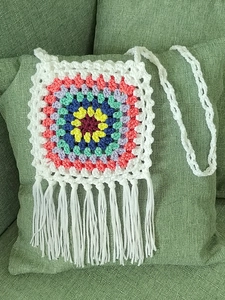 Detail of handmade granny square crochet bag with multi-color patterns and white tassels
