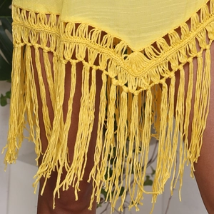 Detail eines gelben Häkelstrands kleides mit V-förmigem Saum und langen Fransenquasten