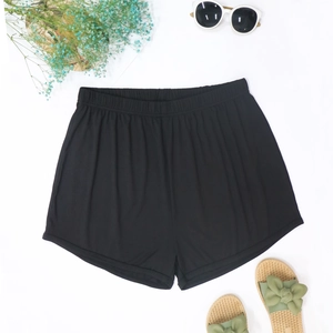 Flat lay of black ribbed beach shorts with summer sunglasses and woven sandals on white