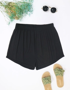 Flat lay of black ribbed summer shorts with straw sandals and beach accessories